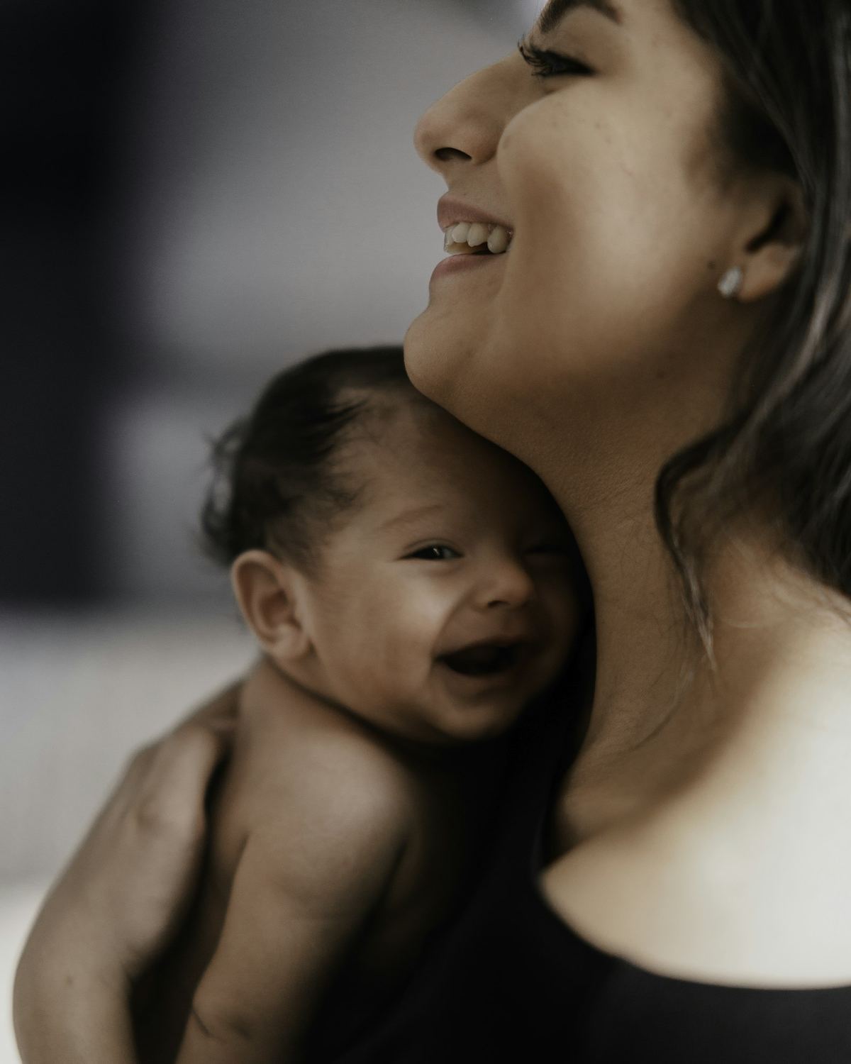 Mãe rindo com o bebê recém-nascido no colo